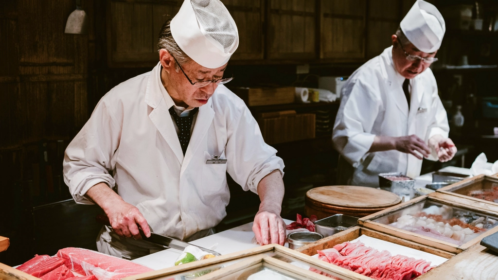 Two sushi chefs in white uniforms preparing sushi at a restaurant counter
